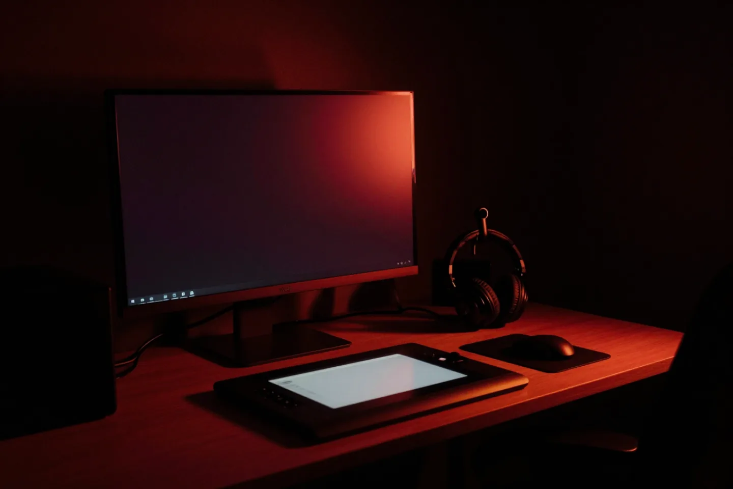 A creative studio workstation: a wide monitor turned away from camera, a graphics tablet, headphones and a warm desk lamp.